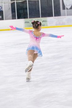 Little girl practicing figure skating on an indoor ice rink.