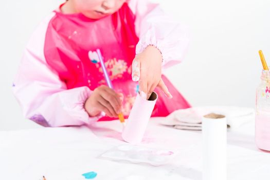 Little girl making a unicorn out of the toilet paper roll and craft paper.