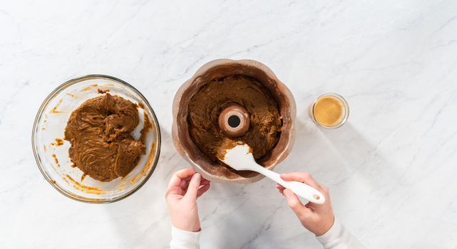 Flat lay. Filling metal bundt cake pan with cake butter to bake gingerbread bundt cake with caramel filling.