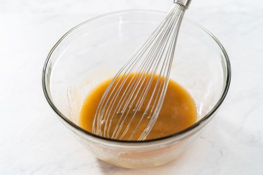 Mixing wet ingredients in a small glass mixing bowl to bake gingerbread bundt cake with caramel filling