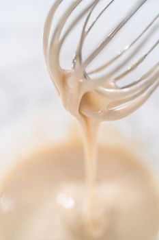 Lemon glaze. Mixing ingredients with a hand whisk in a glass mixing bowl to make lemon glaze.