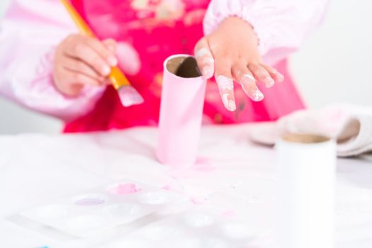 Little girl making a unicorn out of the toilet paper roll and craft paper.