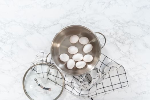 Boiling white eggs in a cooking pot to prepare hard-boiled eggs.