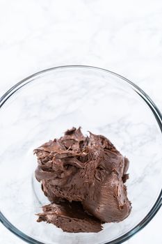 Mixing store-bought chocolate frosting in a mixing glass bowl with a hand mixer.