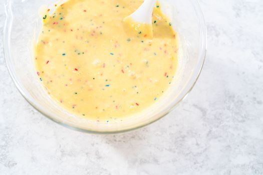 Mixing ingredients in a glass mixing bowl to bake funfettti bundt cake.