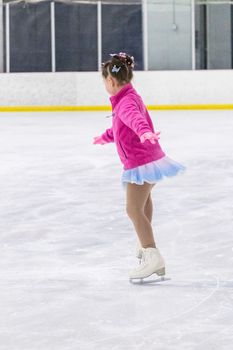 Little girl practicing figure skating on an indoor ice rink.