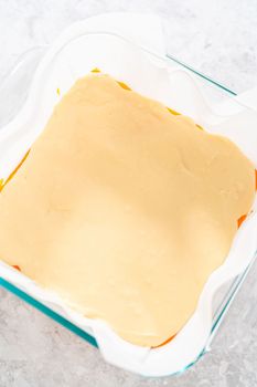 Pouring fudge mixture into the square glass baking pan lined with parchment paper to prepare candy corn fudge.