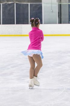 Little girl practicing figure skating on an indoor ice rink.