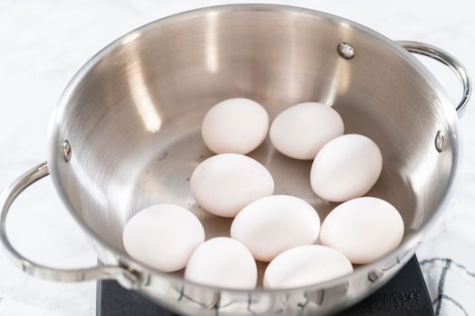 Boiling white eggs in a cooking pot to prepare hard-boiled eggs.