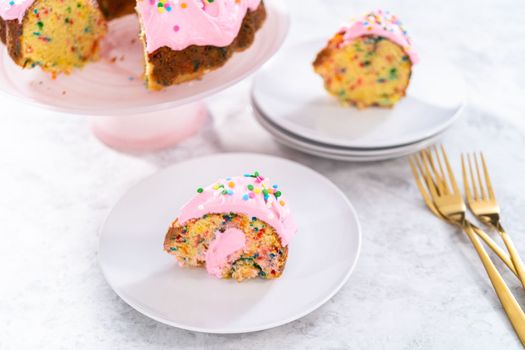 Sliced funfettti bundt cake with pink buttercream frosting on top and buttercream filling inside.