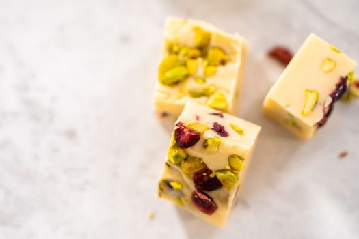 Homemade cranberry pistachio fudge square pieces on a kitchen counter.