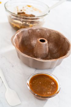 Filling metal bundt cake pan with cake butter to bake gingerbread bundt cake with caramel filling.