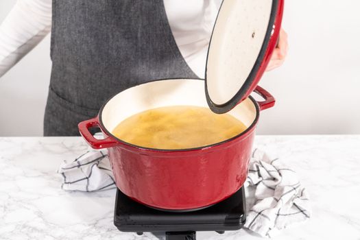 Boiling pasta in an enameled dutch oven to prepare chicken alfredo pasta.