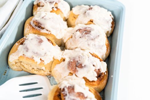 Freshly baked cinnamon rolls with white icing in a blue baking pan.