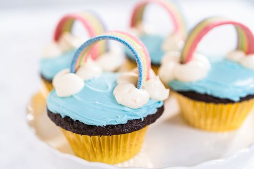 Chocolate cupcakes decorated with blue buttercream frosting and rainbow for unicorn theme birthday party.