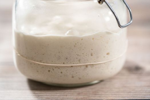 Feeding sourdough starter in a glass mason jar for baking artisan bread.