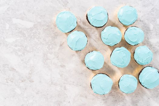 Flat lay. Decorating chocolate cupcakes with buttercream frosting and rainbow candy.