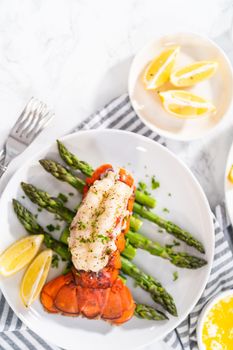 Sering garlic lobster tails with steamed asparagus and lemon wedges on a white plate.