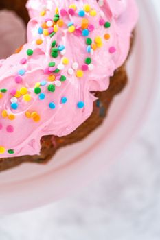 Funfettti bundt cake frosted with pink vanilla buttercream frosting and decorated with rainbow sprinkles.