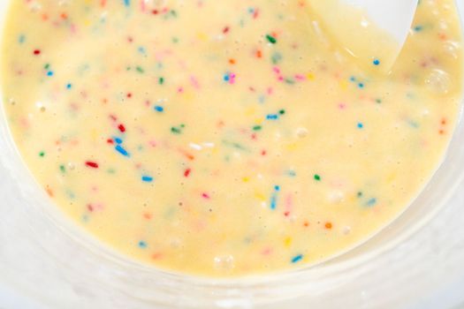 Close up view. Mixing ingredients in a glass mixing bowl to bake funfettti bundt cake.