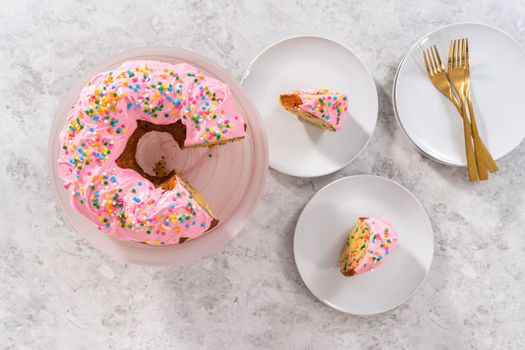 Flat lay. Sliced funfettti bundt cake with pink buttercream frosting on top and buttercream filling inside.