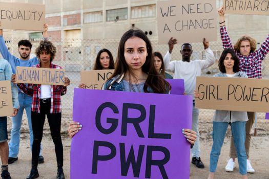 Young woman holding a girl power sign in a demonstration for equality and woman's rights. More protesters in the background. Feminism concept.