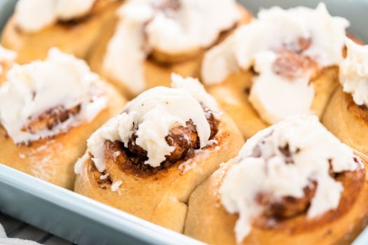 Freshly baked cinnamon rolls with white icing in a blue baking pan.