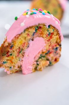 Close up view. Sliced funfettti bundt cake with pink buttercream frosting on top and buttercream filling inside.