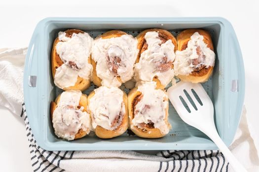 Freshly baked cinnamon rolls with white icing in a blue baking pan.