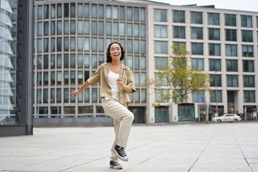 Happy people in city. Upbeat young girl dancing on street in headphones, listening music in headphones.