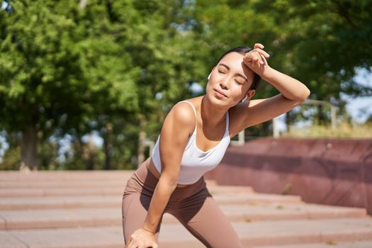 Portrait of sportswoman panting, taking break during jogging training, sweating while running outdoors.