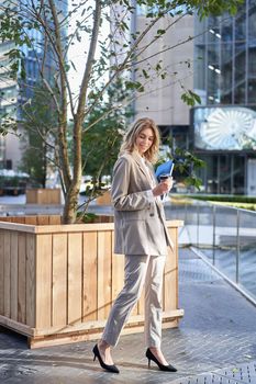 Energized businesswoman drinks coffee, gets takeaway on lunch near office building, standing on street.