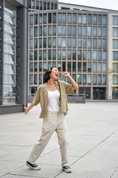 Happy people in city. Upbeat young girl dancing on street in headphones, listening music in headphones.