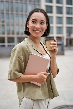 Portrait of asian girl with tablet, drinks coffee on street, walking in city centre.