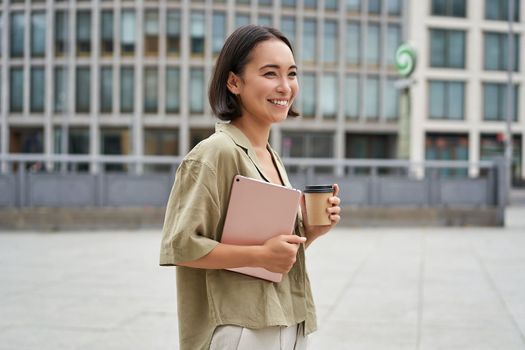 Stylish city girl with tablet, walking on street and drinking takeaway coffee, going to university or work.