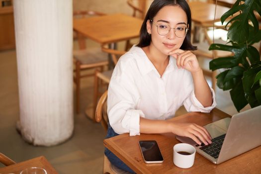 Working female entrepreneur sitting in cafe with laptop, typing on computer, drinking coffee.