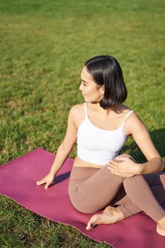 Woman meditating in park on rubber mat, sitting on green lawn and practice yoga, concept of sport and wellbeing.