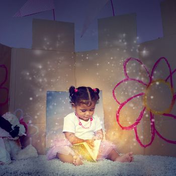 Her very first fairytale. an adorable little girl sitting on the floor and reading a glowing book