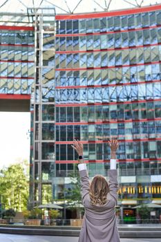 Vertical shot, silhouette of businesswoman raising hands up, celebrating victory, winning and triumphing, looking ecstatic, standing outside on street.