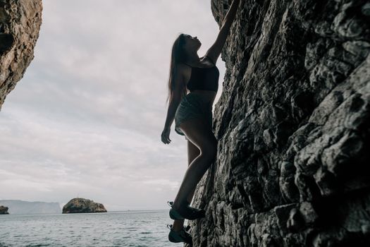 A girl climbs a rock. The athlete trains in nature. Woman overcomes difficult climbing route. Extreme hobby. Tourist woman rock climber hiking on mountains rocks over beautiful sea coast