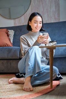 Technology and people. Young stylish asian woman sits at home with her smartphone, texting message, using application on mobile phone.