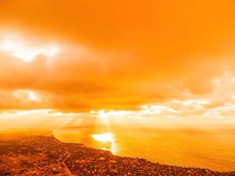 A red burning sunset with the silhouette of a cliff over the sea. Abstract nature summer or spring ocean sea background. Small waves on golden warm water surface with bokeh lights from sun.