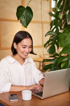 Smiling female manager, freelancer or student sitting with laptop in cafe and working, typing on computer.