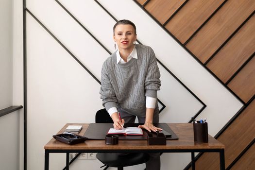 Businesswoman with short haircut in gray sweater at desk in office.