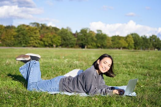 Leisure and people. Happy young woman lying in park on blanket, using laptop, relaxing outdoors and watching videos online on computer.