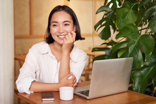 Stylish young freelancer, businesswoman sitting in cafe with laptop and working, drinking coffee.