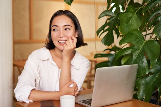 Stylish young freelancer, businesswoman sitting in cafe with laptop and working, drinking coffee.