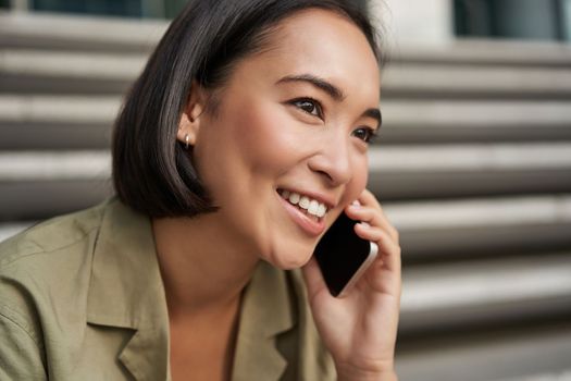 Communication. Young asian woman talking on mobile phone, having a telephone call, using smartphone while sitting on street.