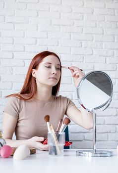 young beautiful woman holding make-up brushes and making up with cosmetics set at home