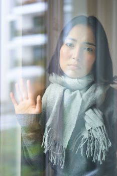 Asian woman feels unwell, stays at home, looks outside window with jealous, distressed face, wants go outside but caught cold.